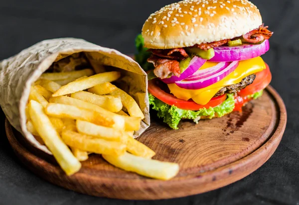 Burger and french fries on a wooden table against black background — Stock Photo, Image