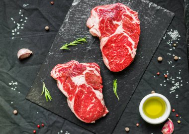 Rib eye beef cow steak meat with spices and herbs against black background clipart