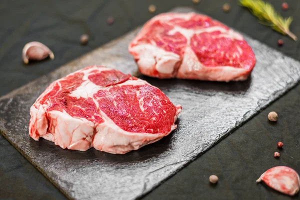 RIB Eye wołowiny krowa stek mięso z przypraw i ziół na czarnym tle — Zdjęcie stockowe
