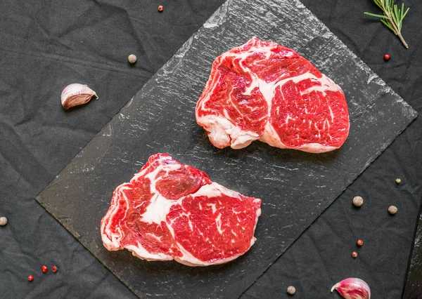RIB Eye wołowiny krowa stek mięso z przypraw i ziół na czarnym tle — Zdjęcie stockowe