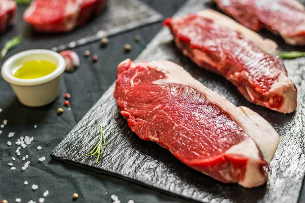 Bistecche di carne bovina con spezie ed erbe su sfondo nero — Foto Stock