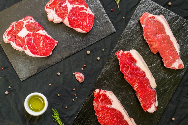 Bistecche di carne bovina con spezie ed erbe su sfondo nero — Foto Stock