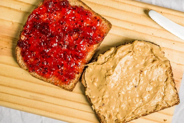 Peanut butter and jelly sandwich on a wooden board against white background