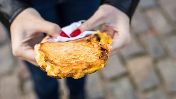 Comer un sándwich con queso fundido a la parrilla y tocino en un mercado de comida callejera — Foto de Stock