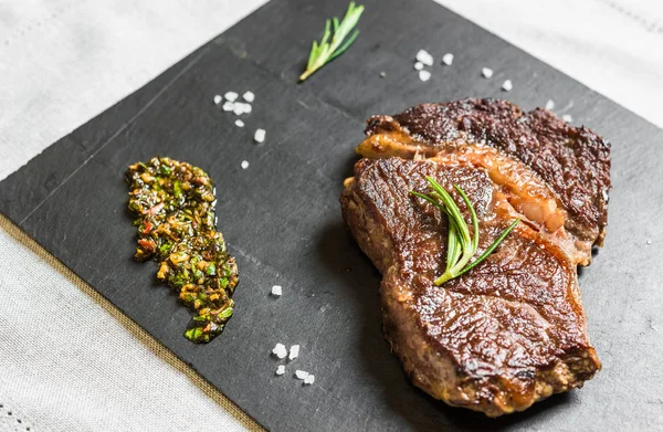 Gegrilde rib eye rundvlees biefstuk met Chimichurri saus tegen zwarte achtergrond — Stockfoto