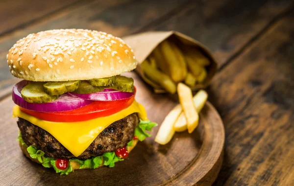 Burger z serem i frytki na drewnianym tle. Smaczne fast food. — Zdjęcie stockowe