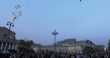 Yukarıda büyük bir avize halata sokakta havada beyaz elbiseli kız acrobat