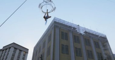 Yukarıda büyük bir avize halata sokakta havada beyaz elbiseli kız acrobat