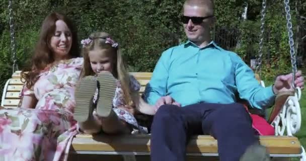 Meisje kind op een schommel met haar ouders — Stockvideo