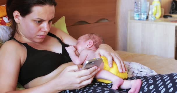 年轻母乳喂养的母亲看新闻智能手机和饲料婴儿 — 图库视频影像