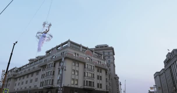 Девушка акробатка в белом платье в воздухе над улицей в большой люстре на веревке — стоковое видео