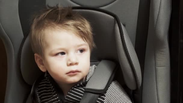 Pikkupoika istuu lastenistuimella autossa. — kuvapankkivideo