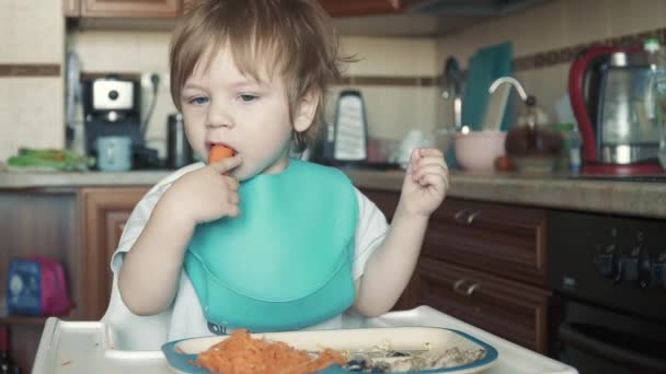 Pojken vid barnbordet äter morötter. — Stockvideo