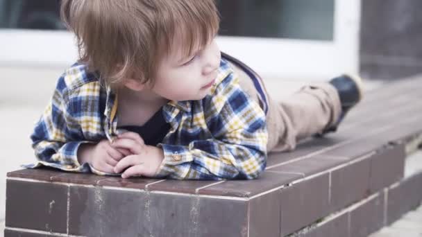 Мальчик лежит на кафельном заборе — стоковое видео