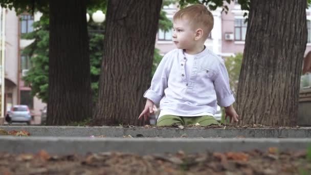 Egy fiú játszik egy városi virágágyásban. — Stock videók