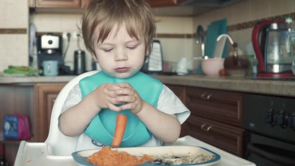 El chico en la mesa de los niños come zanahorias. — Vídeos de Stock