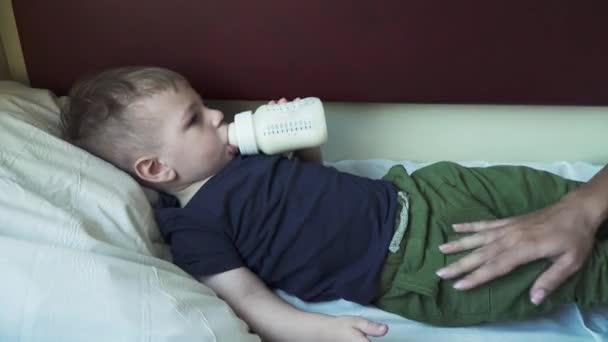 El chico yace en el estante del coche y bebe leche. — Vídeo de stock
