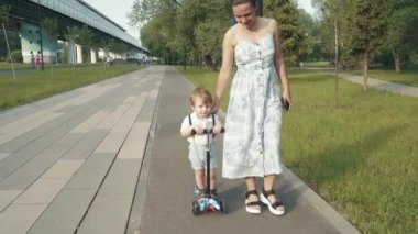 Anne oğluna scooter sürmeyi öğretiyor.