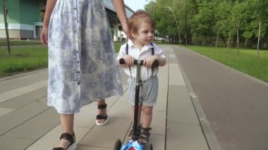 Anne oğluna scooter sürmeyi öğretiyor.