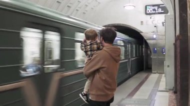 Hareket eden metro trenine karşı babasının kollarında bir çocuk.
