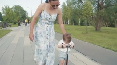 Anne oğluna scooter sürmeyi öğretiyor.