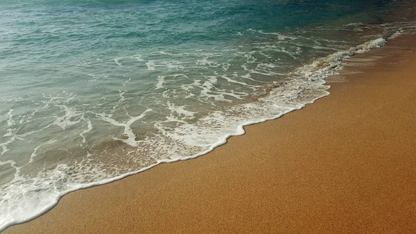Güneşli bir günde kumlu sahilde yumuşak mavi bir dalga..