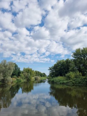 Durgun yüzeyi gökyüzünü yansıtan Irpin Nehri 'nin huzurlu yaz manzarası. Gür, yeşil bankalar kalın otlarla kaplanarak sakin bir doğal manzara yaratıyor. Bu görüntü ahenk, doğa ve huzur dolu bir rahatlama hissi uyandırıyor..