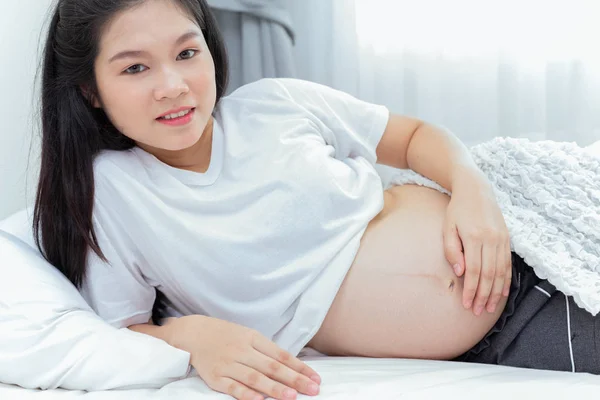 Mujer embarazada joven durmiendo en la sonrisa dormitorio y mirando ca — Foto de Stock