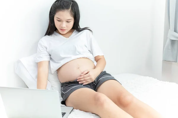 Портрет беременной азиатки с помощью ноутбука на кровати, серфинг — стоковое фото