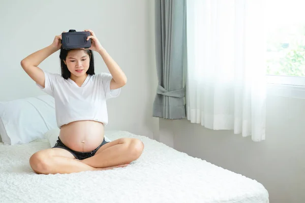 Embarazada mujer asiática está usando un dispositivo de realidad virtual sentado — Foto de Stock