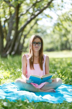 güzel bir genç beyaz kadın açık bir kitap okuma portresi. Çimenlerin üzerinde oturan