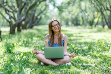 Lotus pozisyonda onu laptop ile parkta oturan öğrenci