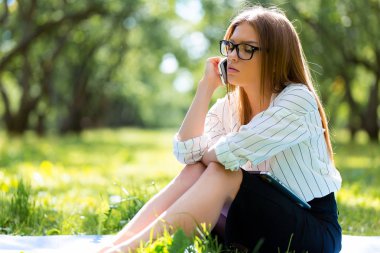 Parkta çimlere oturup telefonda konuşurken kız