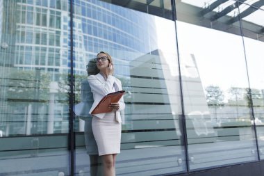 Gri ofis içinde genç kadın elinde belgeler klasörüyle tutar. İş kadını iş merkezi yanında ayakta
