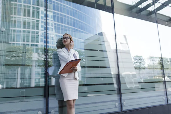 The young woman in gray office dress holds in hand folder with documents. Businesswoman standing next to the business center