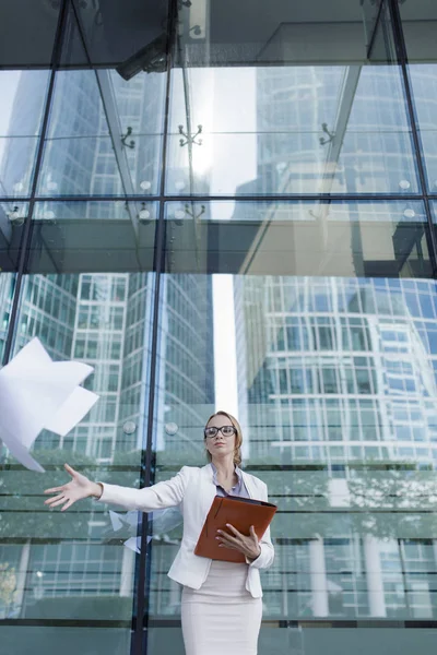 The young woman in gray office dress holds in hand folder with documents. Businesswoman standing next to the business center