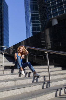 Onun smartphone ile gökdelenler arasında adımları üzerinde oturan güzel kadın