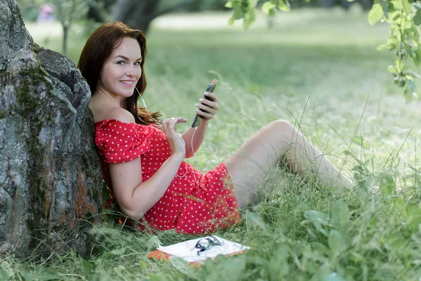 Młoda Ładna Kobieta Siedzi Trawie Pod Drzewem Jej Smartfona — Zdjęcie stockowe