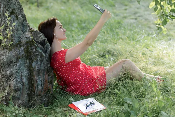 Jonge Vrouw Zittend Het Gras Onder Boom Met Haar Smartphone — Stockfoto
