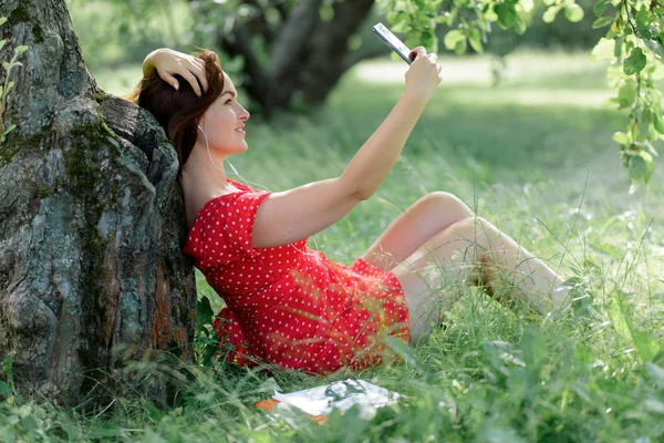 Jonge Vrouw Zittend Het Gras Onder Boom Met Haar Smartphone — Stockfoto