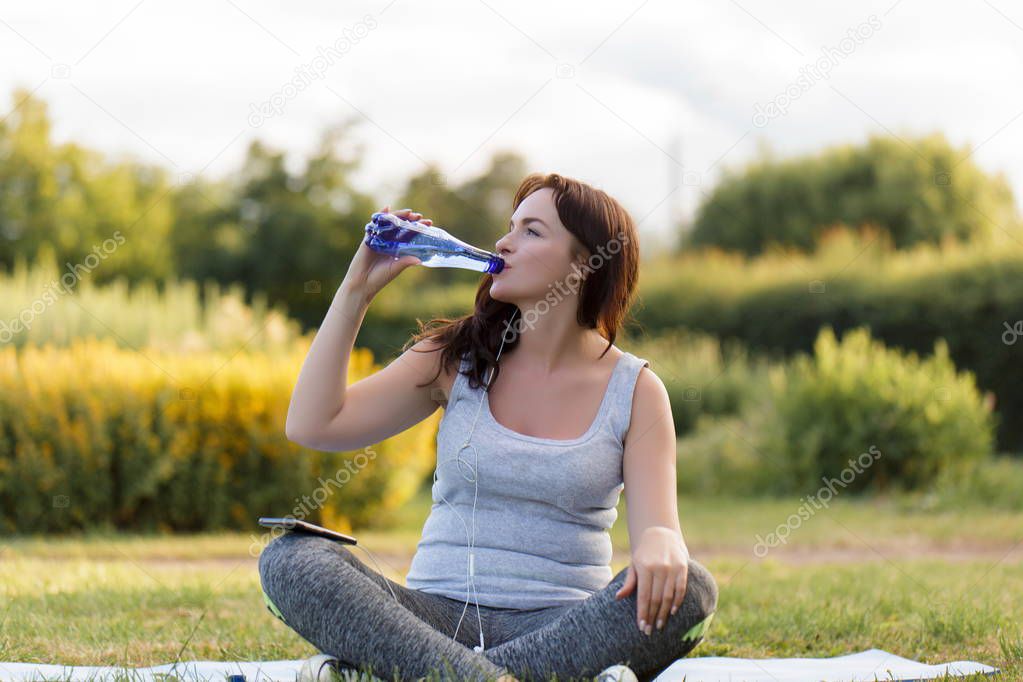 Fitness young beautiful girl drinking water after exercising at the park