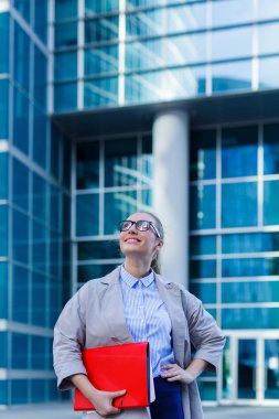 Gri ofis içinde genç kadın elinde belgeler klasörüyle tutar. İş kadını iş merkezi yanında ayakta