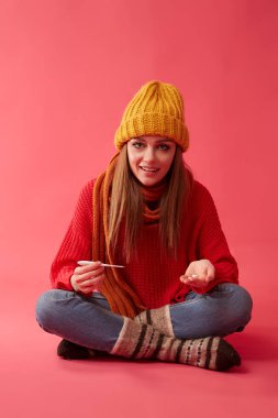 Hasta bir kadına sarı şapkalı bir tıbbi bir termometre ve hapları onun elinde tutar. Pembe arka plan görüntü