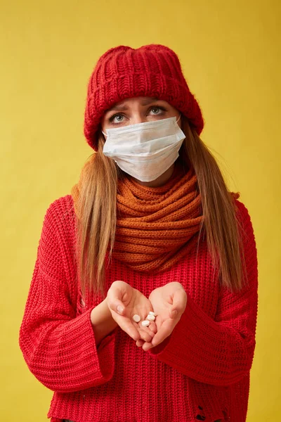 Sick woman in a medical mask holding pills in her hands Image on yellow background.