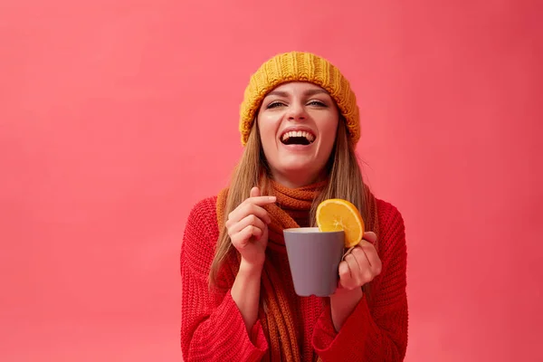 Красивая девушка в теплом уютном свитере держит горячий напиток с апельсином. Красный фон. Студия — стоковое фото
