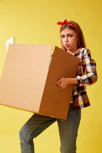 İnsanlar hareketli yeni yer ve onarım kavramı - karton kutu tutan genç kadın. Sarı arka plan.