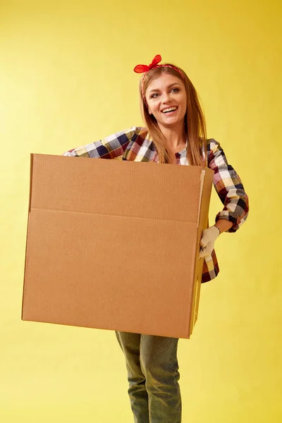 Люди переезжают новое место и концепция ремонта - молодая женщина держит картонную коробку. Желтый фон . — стоковое фото