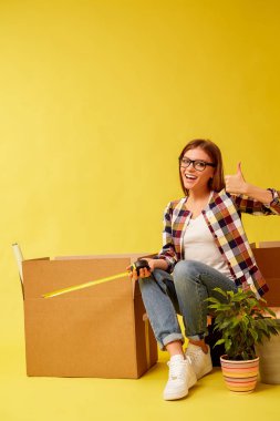 Taşıma kutuları arasında bir araç kutusu üzerinde oturan bir ölçüm bandı tutan genç kadın