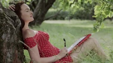 Ağaç altında çim üzerinde oturan ve notlar yazma genç kız