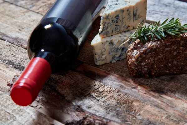 Bottle of red wine on rough wood surface with aromatic blue cheese and bread with walnuts and rosemary — Φωτογραφία Αρχείου